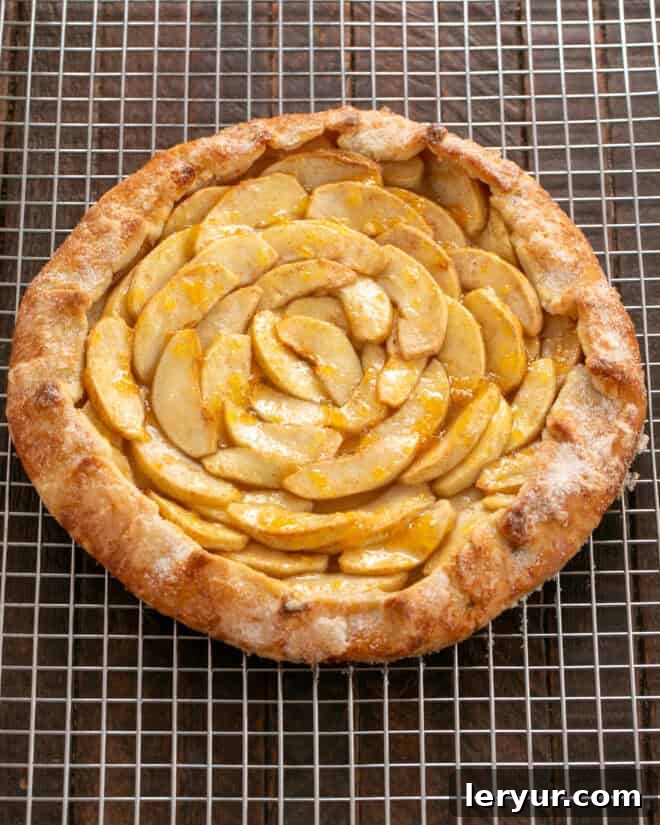 Baked apple galette cooling on a rack, with a pastry brush poised to glaze the apples with jam or jelly for a beautiful sheen.
