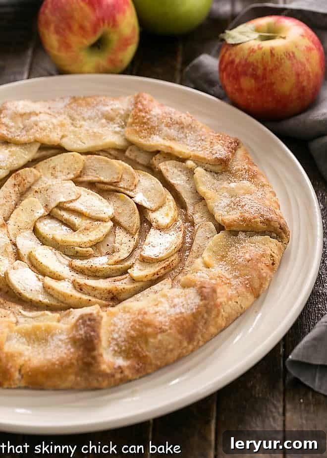 Rustic Apple Tart on a white plate with fresh apples blurred in the background, highlighting the dessert's natural beauty.