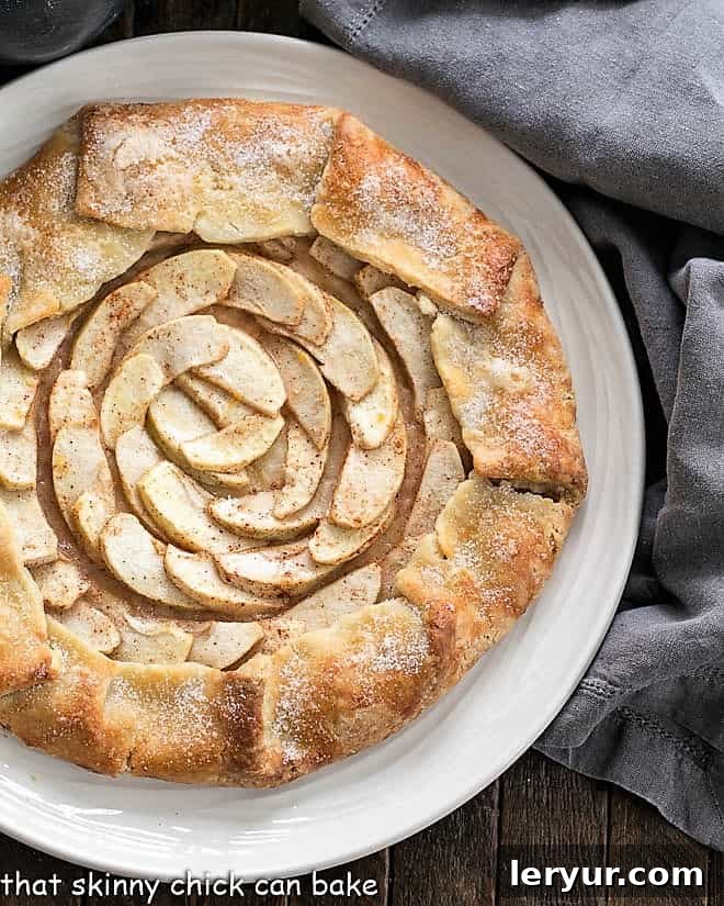 Partial overhead view of a baked Apple Tart on a white serving plate, showing its golden crust and caramelized apples.