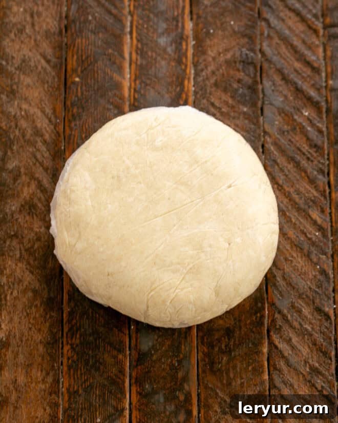 Apple galette dough formed into a disk and wrapped in plastic, ready to chill in the refrigerator.