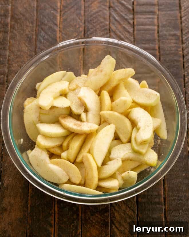 Peeled, sliced, sweetened apples in a clear glass bowl, seasoned with cinnamon, sugar, and lemon juice.