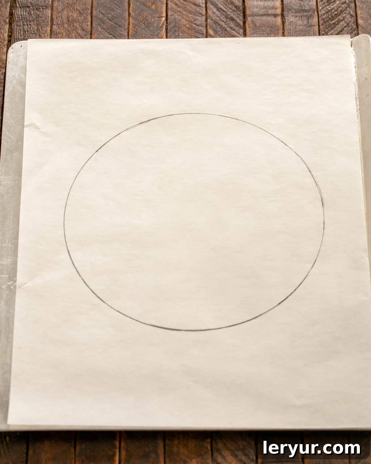 Parchment paper with a drawn 9-inch circle acting as a template for the pavlova on a baking sheet.