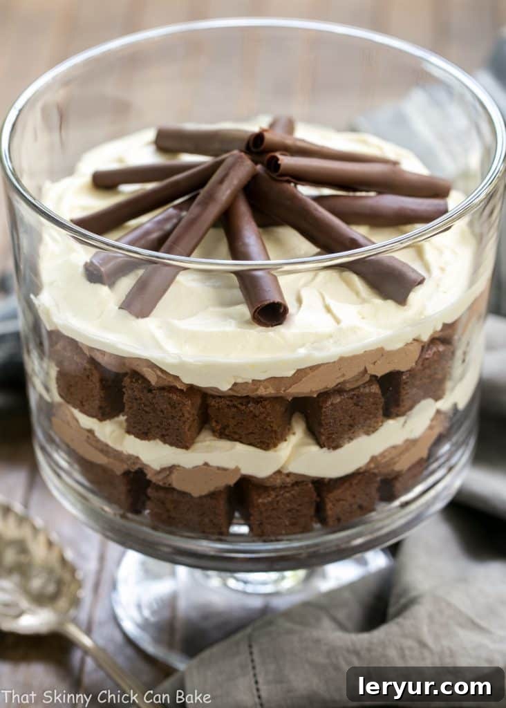 A stunning side profile view of the Fudgy Brownie Trifle with Chocolate Mousse in a clear glass trifle bowl, showcasing all three distinct layers and the beautiful chocolate curls on top. This image highlights the dessert's elegant presentation.