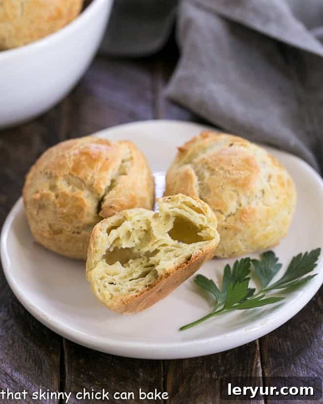 Blue Cheese Gougères - a twist on the classic pâte à choux pastry based cheese puffs with blue cheese and a pinch of cayenne! Absolutely irresistible! Cheese puffs on a small white plate with one broken open to expose the airy, cheesy interior.