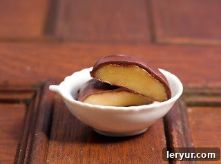 A chocolate covered caramel, cut in half to reveal its soft center, in a small white bowl