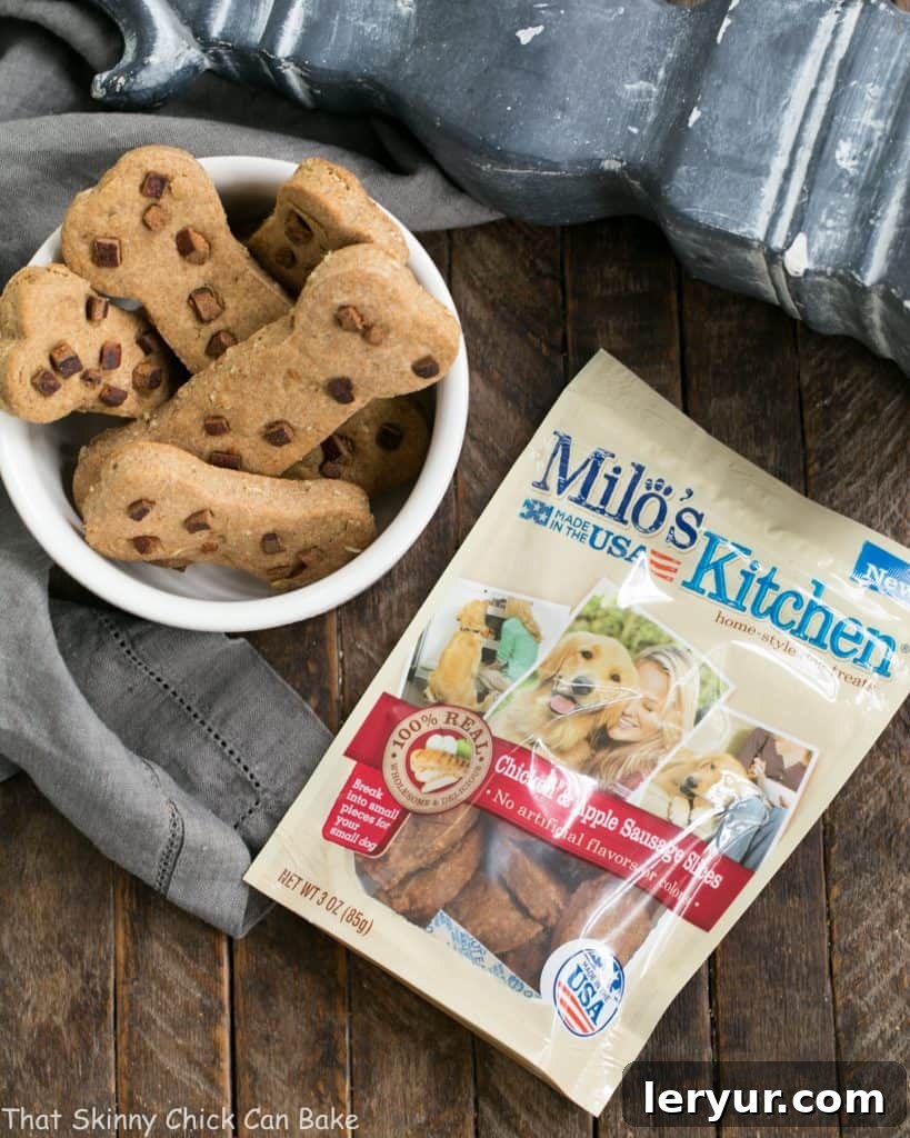 Two tempting homemade peanut butter dog bone treats rest in a pristine white bowl, accompanied by a vibrant packet of Milo's Kitchen Grilled Chicken Strips, highlighting the quality ingredient addition.
