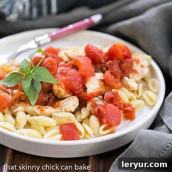 Chicken Feta Casserole - A fabulous casserole chock full of tomatoes, garlic, feta and herbs! A close-up of Chicken Feta Casserole in a white bowl garnished with fresh basil, showcasing its rich texture and vibrant colors.