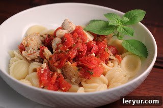 Chicken Feta Casserole - an easy, flavorful weeknight entree A serving of Chicken Feta Casserole in a white bowl, elegantly garnished with a sprig of fresh basil.