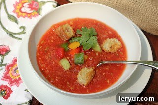 Real Spanish Gazpacho - a refreshing tomato based cold soup that's perfect in the summer Gazpacho in a white bowl with toppings and a spoon.