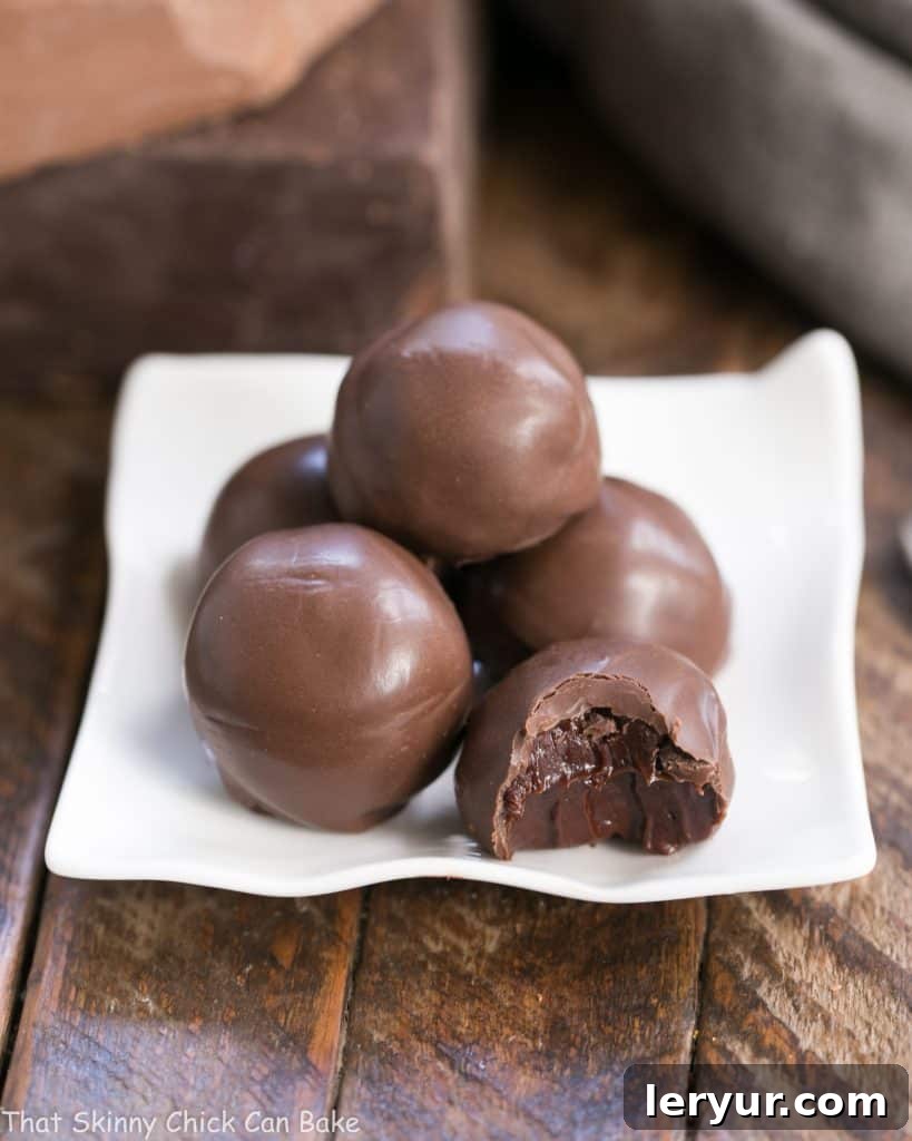 Chocolate Frangelico Truffles - Exquisite truffles flavored with hazelnut liqueur plus a guide for tempering chocolate Close-up of a Chocolate Frangelico Truffle on a square white plate, with one truffle cut open to reveal its creamy ganache filling.