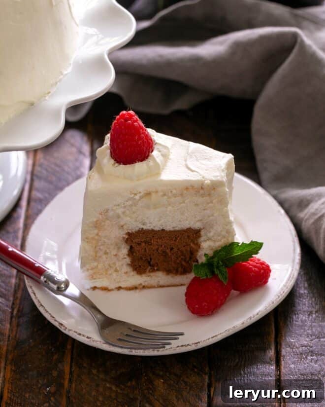 A beautifully frosted and sliced angel food cake, showing the chocolate mousse filling, garnished with fresh raspberries.