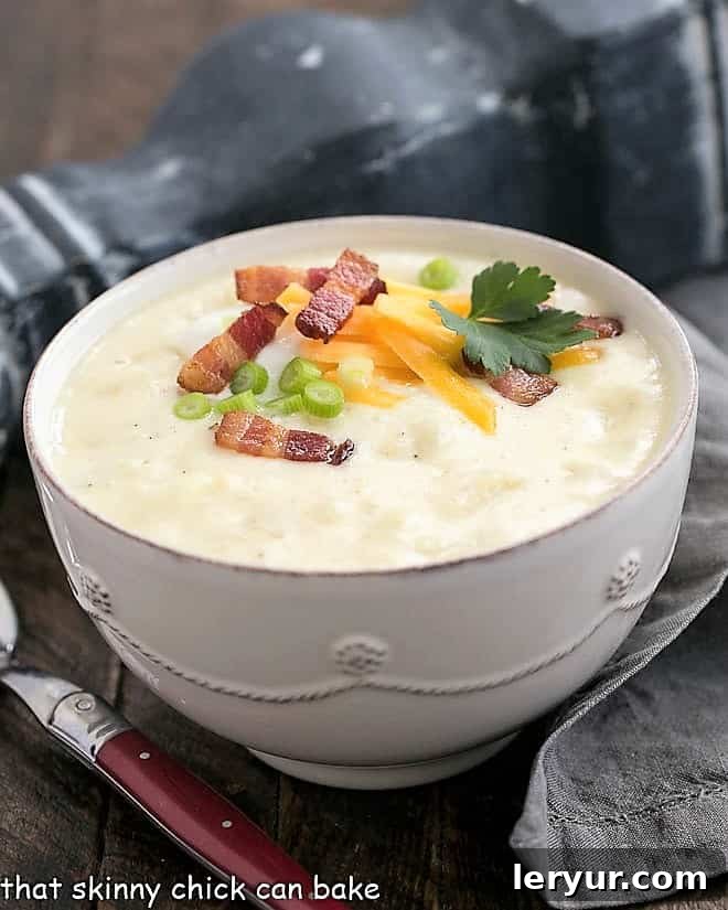 A rustic white terrine filled with creamy Loaded Baked Potato Soup, adorned with a medley of melted cheese, crispy bacon, and vibrant chives, ready for serving.