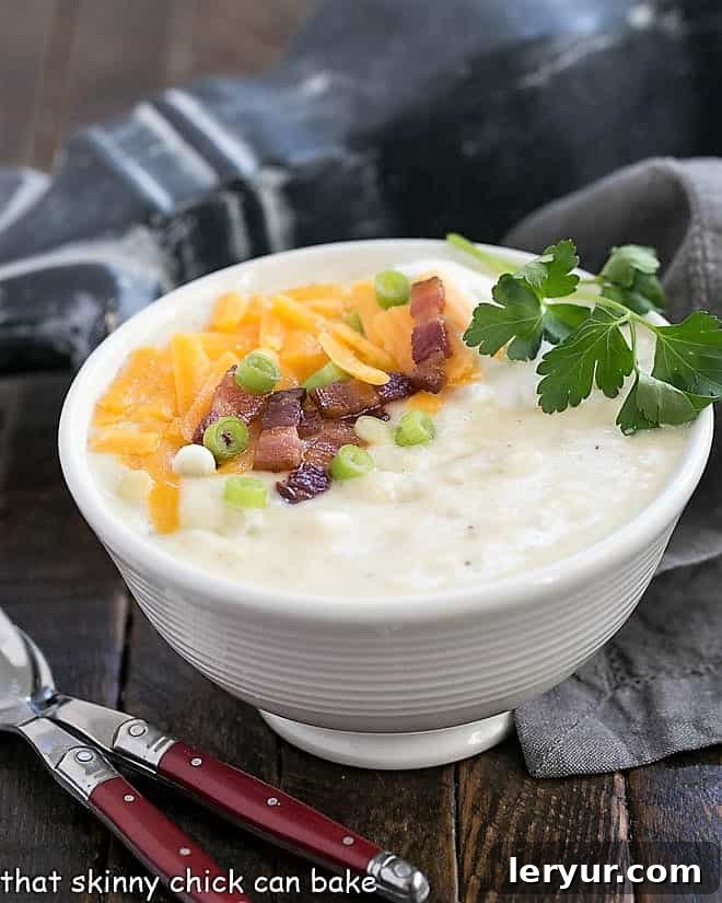 A captivating side view of a white ceramic soup bowl brimming with Loaded Baked Potato Soup, accompanied by two elegant red-handled soup spoons, highlighting its inviting texture.