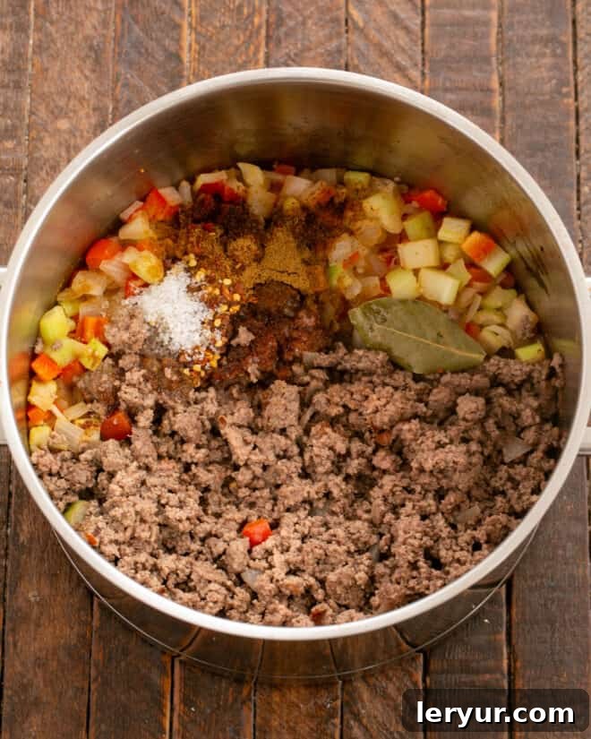 Adding ground beef and seasonings to sautéed vegetables.