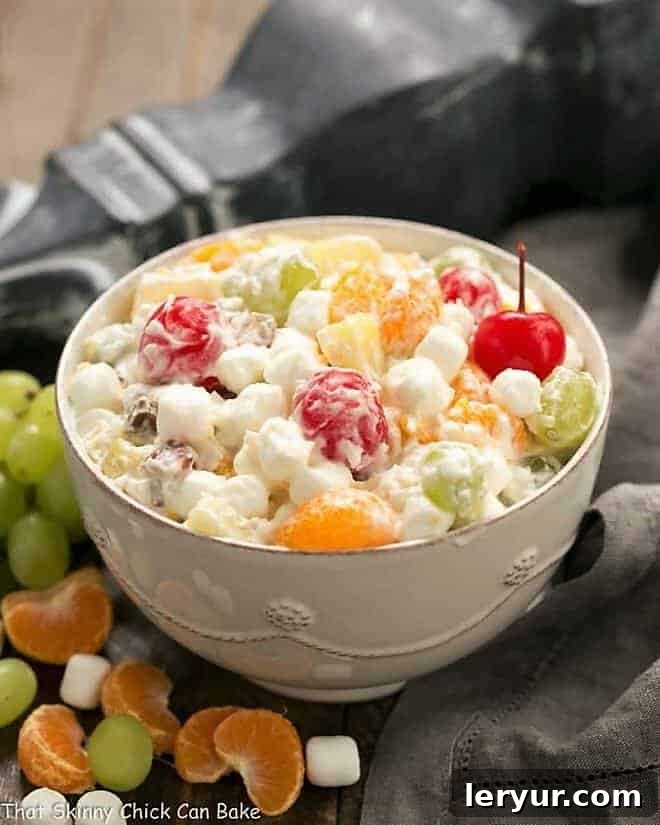 The Best Ambrosia Salad {No Cool Whip} in a pristine white ceramic bowl, garnished with fresh fruit and coconut flakes.