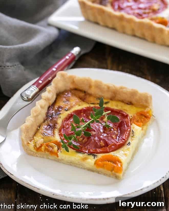 Sun-Kissed Tomato Gruyère Tart 2 A beautifully presented Tomato Gruyere Tart slice on a white plate with a red handle fork, highlighting its layers and inviting texture.