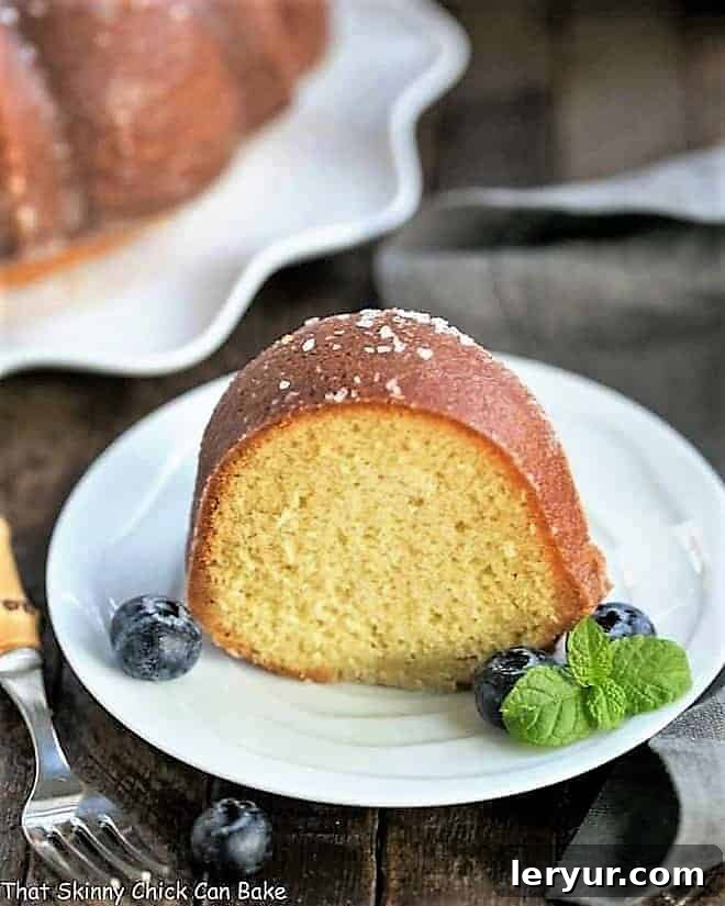 Vanilla Bundt Cake - A simple, versatile butter cake that can be served in so many ways! A perfectly sliced Kentucky Butter Bundt Cake on a white dessert plate, adorned with fresh blueberries and a delicate sprig of mint, showcasing its moist texture.