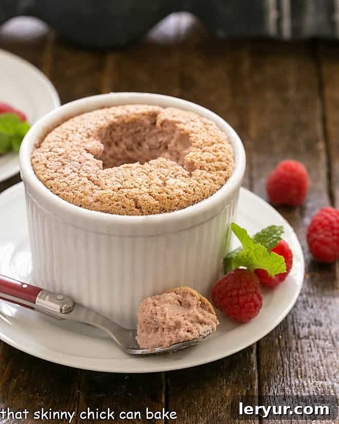 A delectable raspberry souffle with a spoonful taken out, resting in front of its ramekin, highlighting its irresistible texture.