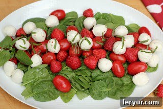 Strawberry Caprese Salad 3 Close-up shot of the Mozzarella, Tomato and Strawberry Salad on a white platter, highlighting the fresh bocconcini, halved strawberries, and grape tomatoes, all glistening with dressing and adorned with basil.