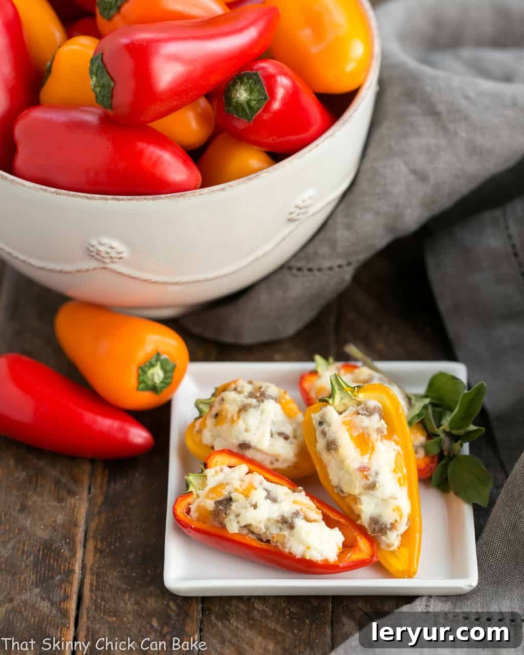 Cream Cheese Stuffed Mini Peppers with Sausage - An unbelievably easy, incredibly flavorful appetizer perfect for any occasion, from casual game nights to elegant dinner parties! Discover your new favorite go-to recipe for entertaining. A square plate filled with golden-brown Cream Cheese Stuffed Mini Peppers with Sausage, accompanied by a small bowl of fresh, vibrant mini peppers.