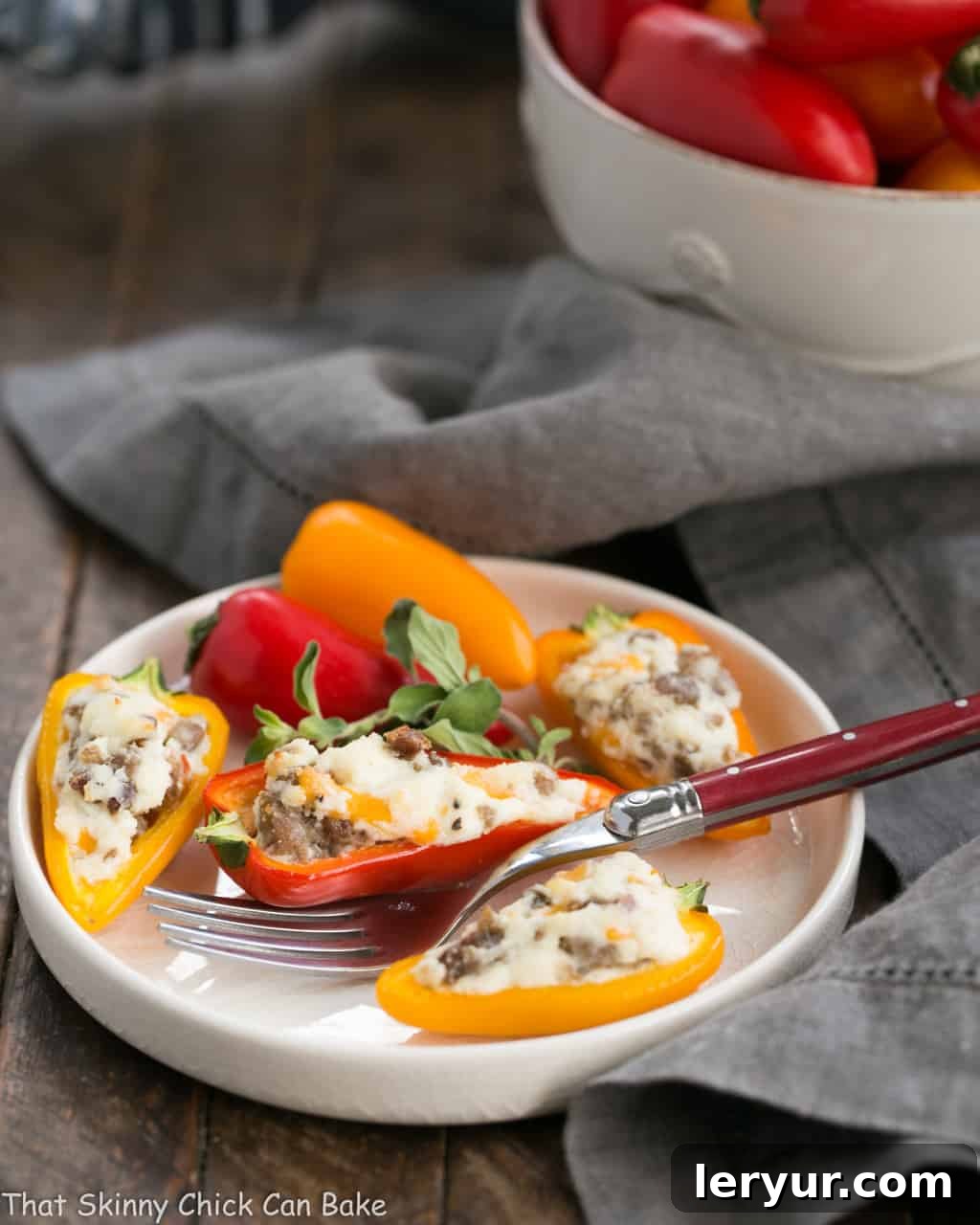 Cream Cheese Stuffed Mini Peppers with Sausage - A simple, yet elegant appetizer that’s always a crowd-pleaser for any gathering or casual meal. A close-up shot of perfectly baked Cream Cheese Stuffed Mini Peppers with Sausage on a round white plate, with a red-handled fork resting beside it.
