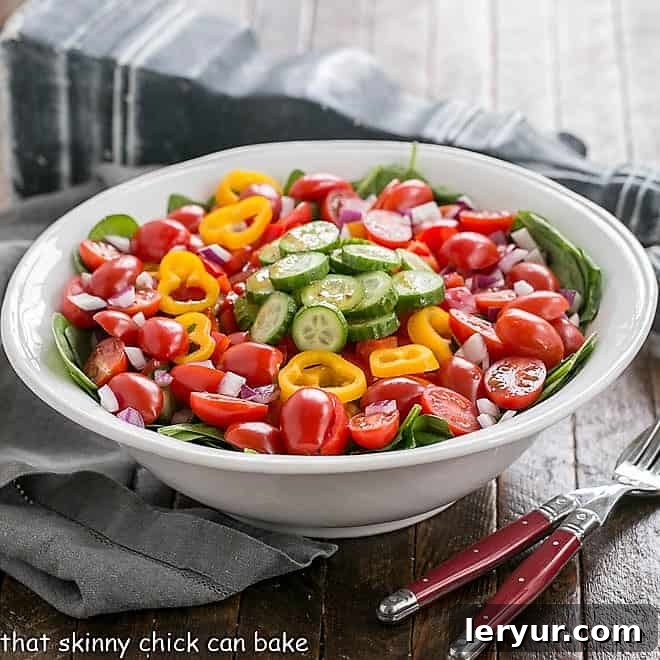 Gazpacho Spinach Salad - a refreshing vegetable salad with a piquant red wine vinaigrette Gazpacho Spinach Salad in a white bowl with red-handled serving utensils.