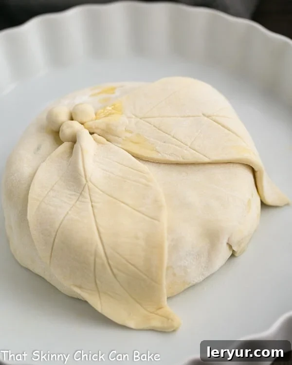 Cranberry Brie en Croute wrapped in puff pastry with decorative cuts before baking, on a parchment-lined baking sheet.