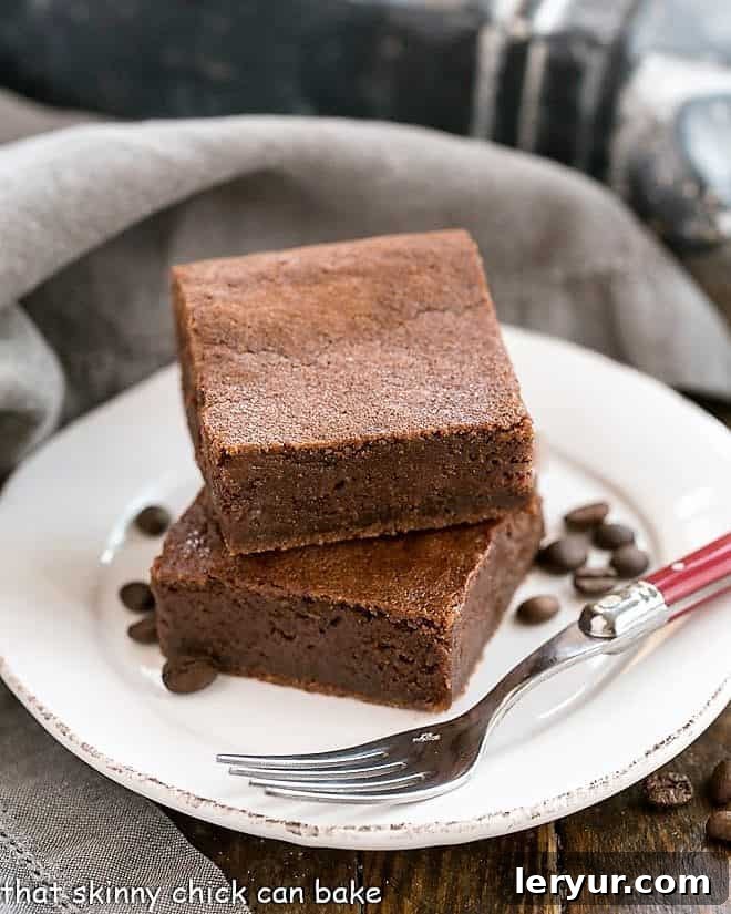 Fudgy Kahlua Brownies on a round white plate, artfully surrounded by coffee beans with a fork resting beside them
