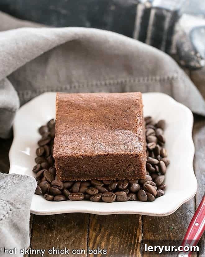 Decadent Kahlua Brownies presented on a pristine square white plate, nestled amongst roasted coffee beans for a striking visual contrast