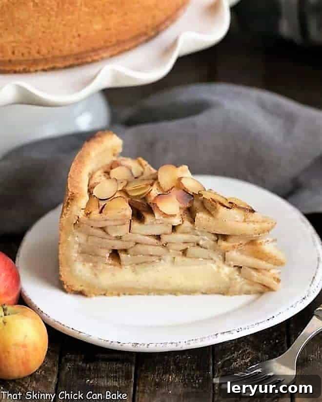 Cream Cheese Apple Torte - A buttery crust is topped with sweetened cream cheese, loads of cinnamon spiced apples, then sliced almonds A stunning Cream Cheese Apple Torte on a pristine white dessert plate, elegantly presented on a cake stand, with fresh apples and a fork nearby, showcasing its beautiful layers.