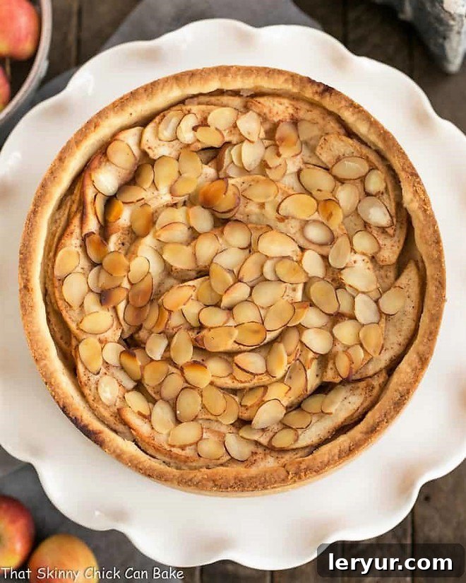 Cream Cheese Apple Torte - A buttery crust is topped with sweetened cream cheese, loads of cinnamon spiced apples, then sliced almonds A beautiful Cream Cheese Apple Torte on a ruffled white cake stand, captured from an appealing overhead perspective, showcasing its layers and perfectly baked crust.
