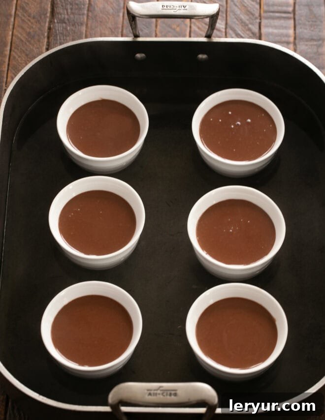 Pouring strained custard into ramekins and adding hot water to the baking dish.