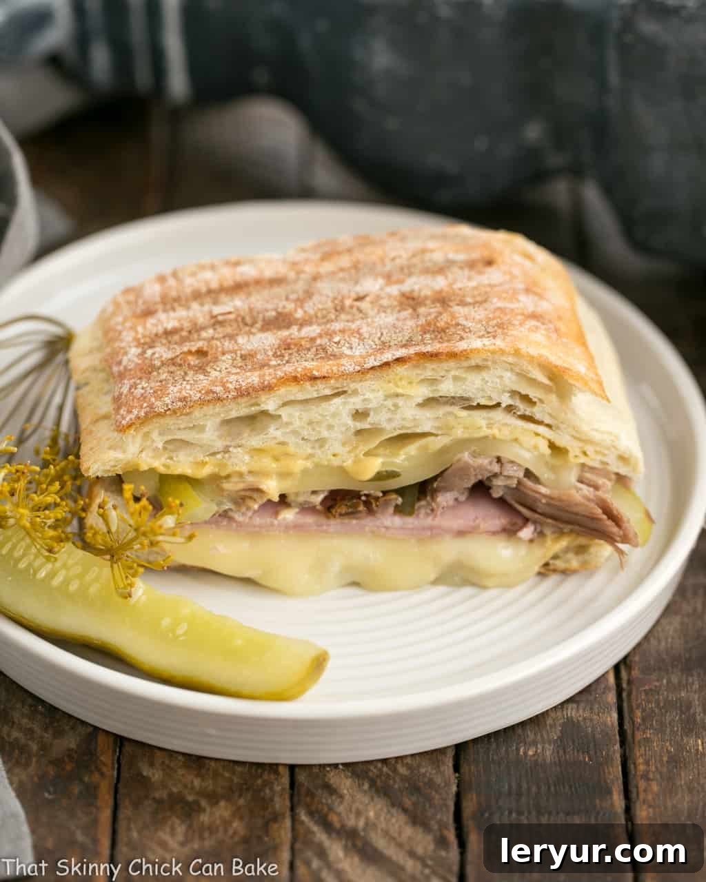 Ciabatta Cubano Sandwich Recipe on a round plate with a dill pickle, showcasing the grilled exterior and rich filling.