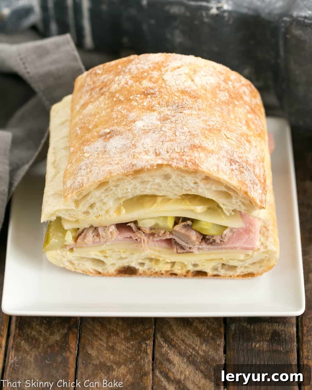 Side view of Ciabatta Cubano Sandwich Recipe before cooking, showing layers of meat, cheese, and pickles.