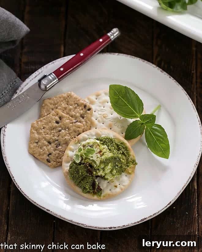 Layered Pesto Dip is a wonderful appetizer with pesto, cream cheese, provolone and sun-dried tomatoes. Perfect on crackers for any occasion! Overhead view of Layered pesto dip on a cracker on a white plate