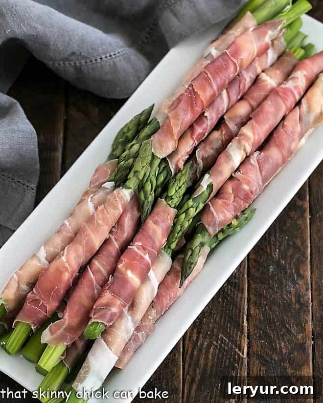 Elegantly arranged stacks of prosciutto wrapped asparagus on a white serving tray, ready for guests.