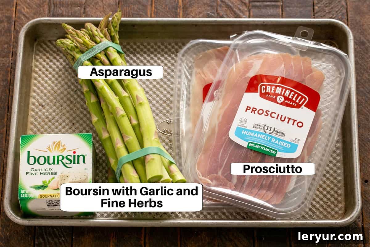 Individual ingredients for Prosciutto Wrapped Asparagus with Boursin displayed on a metal sheet pan: fresh asparagus, a package of prosciutto, and a container of Boursin cheese.