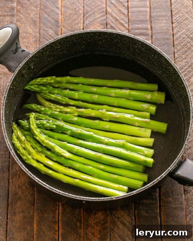Prosciutto Wrapped Asparagus Step 1: Fresh asparagus spears are blanched, drained, and cooling on a surface, ready for the next step.