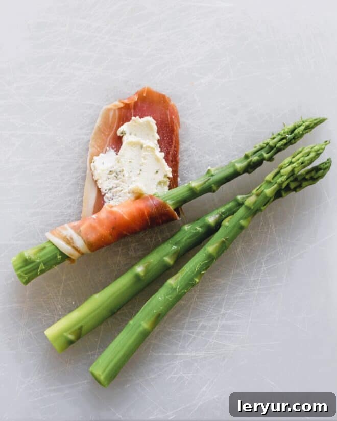 Prosciutto Wrapped Asparagus Step 3: A blanched asparagus spear is neatly wrapped with a Boursin-covered prosciutto slice, creating a delicate spiral.