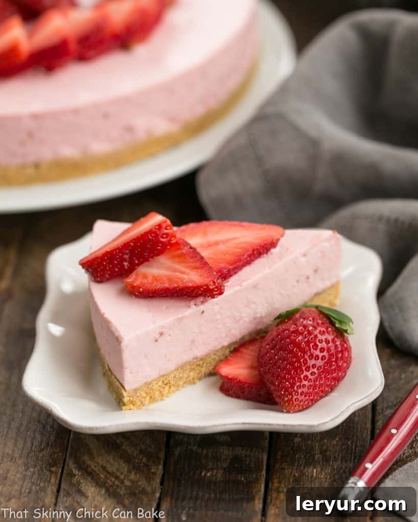 A perfect slice of No-Bake Strawberry Cheesecake on a pristine white dessert plate, showcasing its creamy pink filling and crumbly crust.