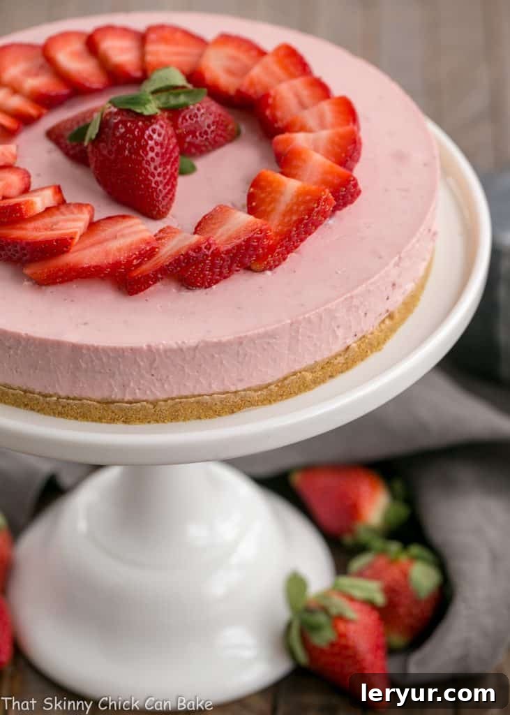 An overhead view of the No-Bake Strawberry Cheesecake on a cake stand, revealing its smooth, enticing top and rich pink hue.