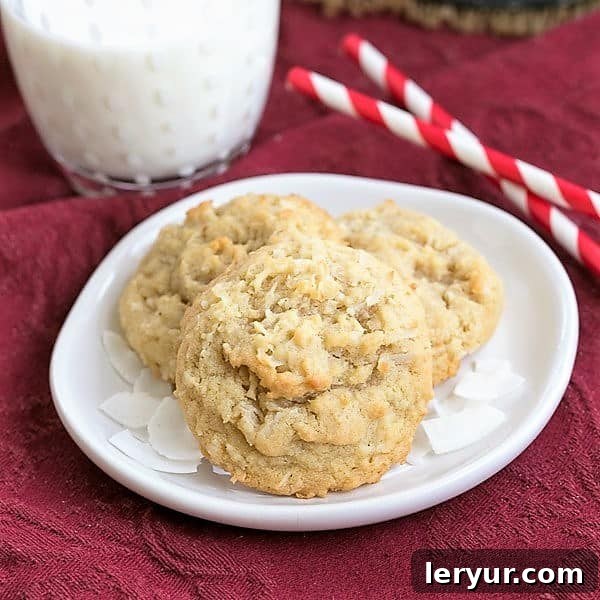 Chewy Coconut Cookies - Buttery cookies chock full of coconut! Four chewy coconut cookies arranged on a white plate, accompanied by a glass of milk and straws, inviting you to enjoy a delightful treat.