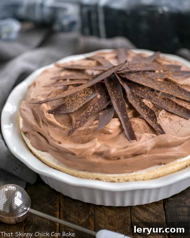 Close-up of Chocolate Velvet Pie with Meringue Crust in a white pie plate, artfully garnished with delicate chocolate shards and a light dusting of cocoa powder.