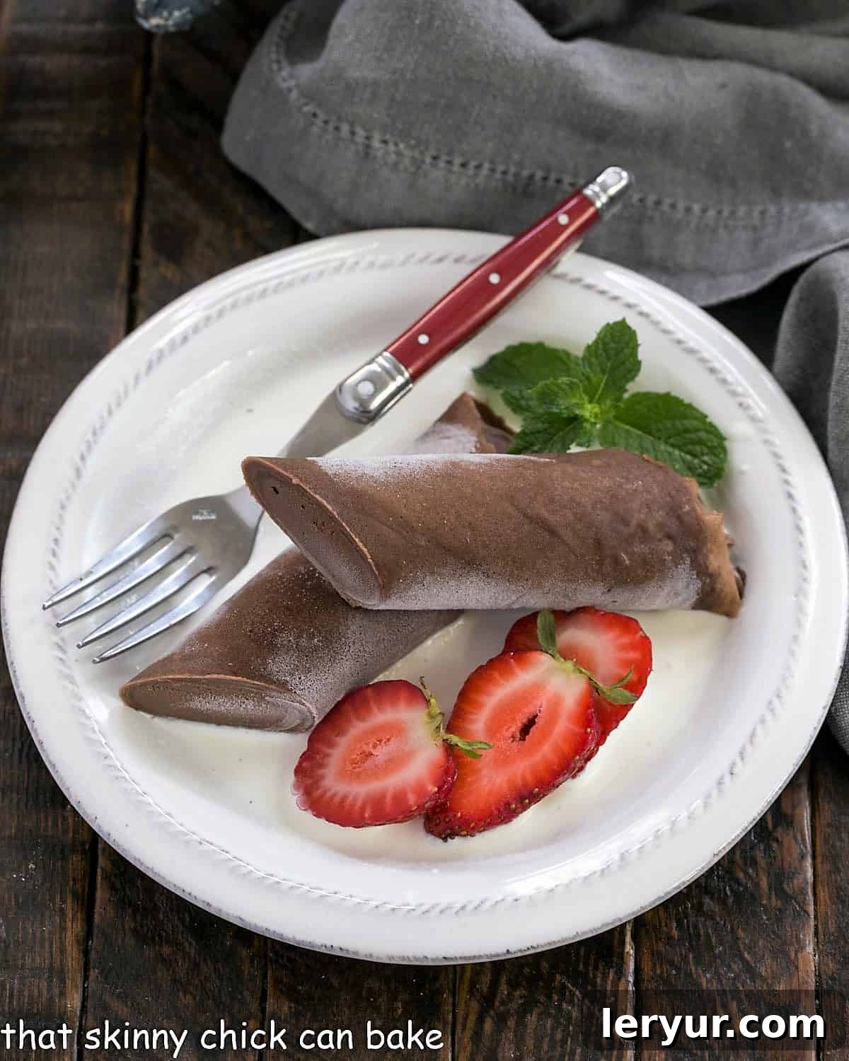 Overhead view of frozen chocolate crepe and berries on a white plate with a red handle fork.