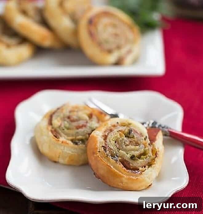 A beautifully presented Prosciutto, Gruyere and Basil Pinwheel on a white plate, ready to be eaten with a small fork beside it.