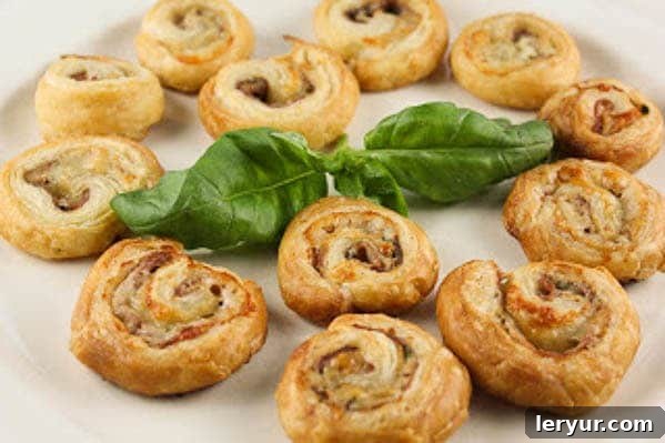 Prosciutto Gruyère Pinwheels made with homemade puff pastry A cluster of golden Prosciutto Gruyère Pinwheels resting on a pristine white serving tray, garnished with a fresh sprig of basil.