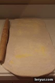 Homemade puff pastry for pinwheel appetizer Close-up of puff pastry being rolled out, showing slight imperfections where butter has begun to emerge, a common occurrence with homemade dough.