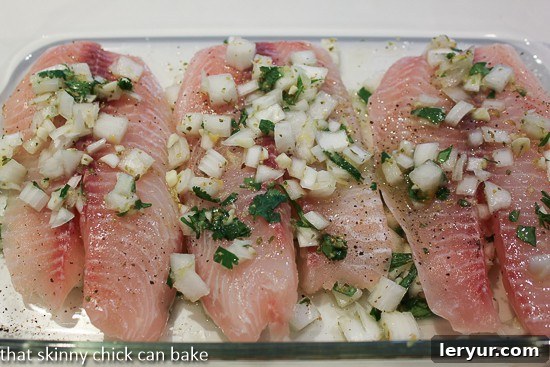 A close-up view of fresh white fish fillets marinating in a vibrant, zesty citrus and herb mixture, nestled in a clear glass baking dish, signaling preparation for a flavorful grilled meal.