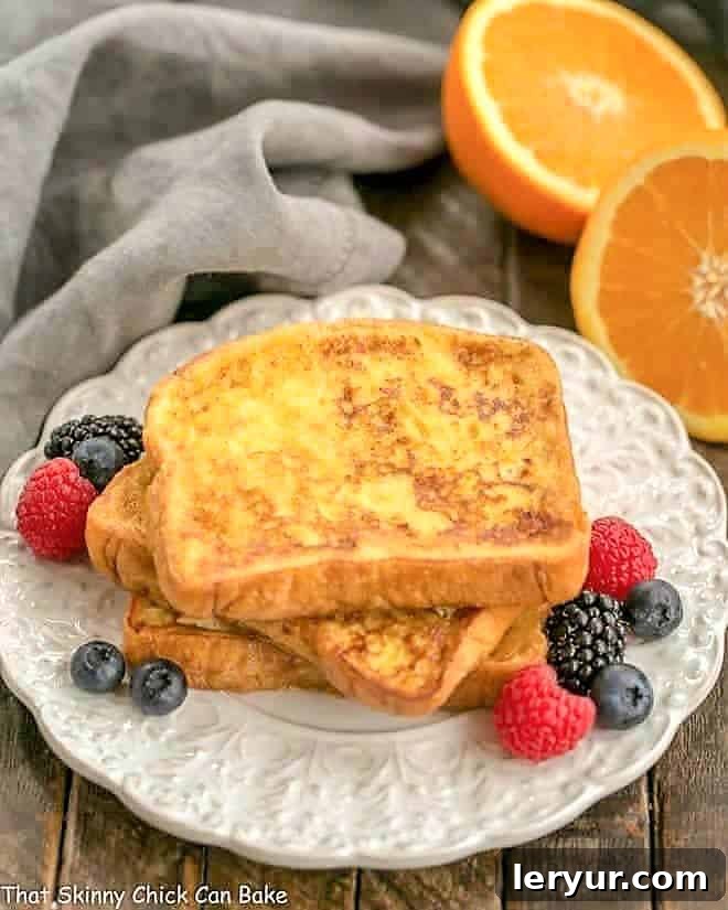 Elegant Grand Marnier French Toast - a gourmet brunch dish with orange liqueur and zest Stacked Grand Marnier French Toast on a decorative plate, garnished with fresh berries and a dusting of powdered sugar.