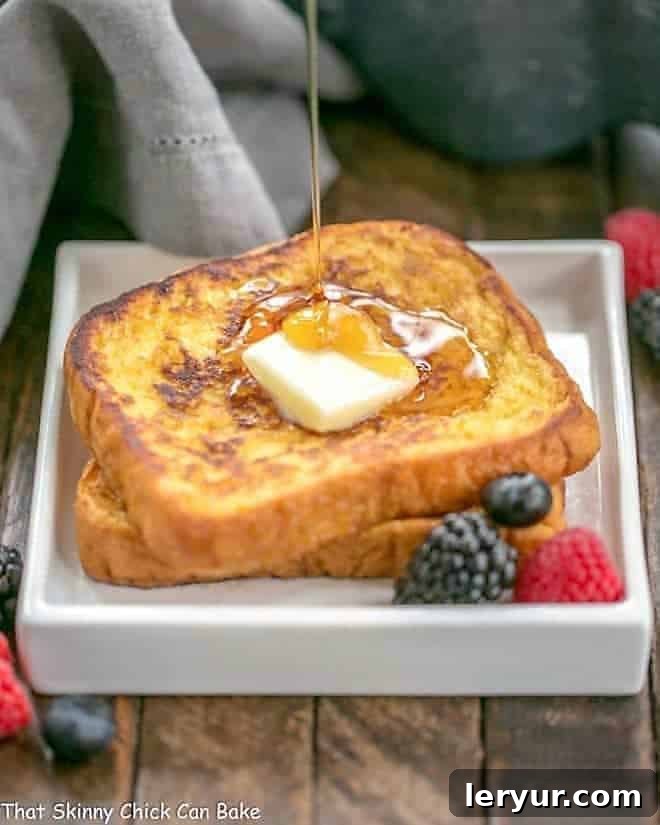 Decadent Grand Marnier French Toast - a double dose of orange in this gourmet breakfast dish Grand Marnier French Toast on a square white plate with a stream of syrup pooling onto the surface and fresh berries.